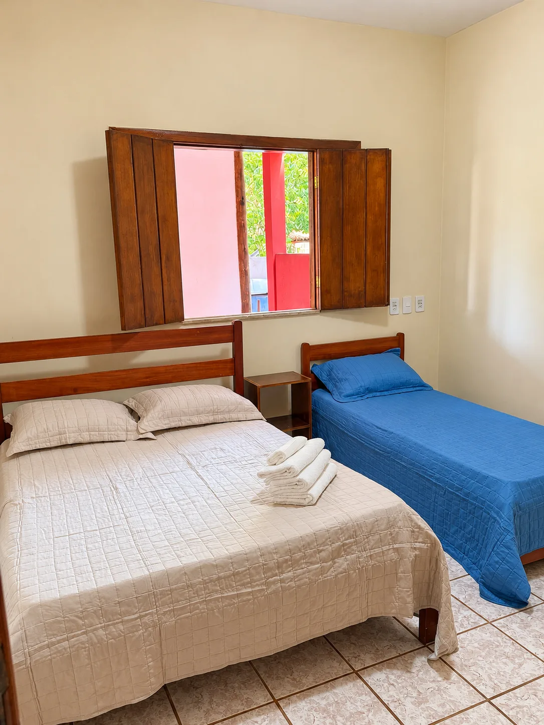 Quarto com uma cama de casal e uma de solteiro, com janela de madeira